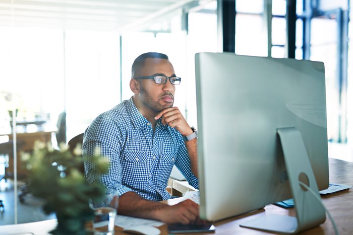 A man at a computer screen is looking closely at the work on his monitor.