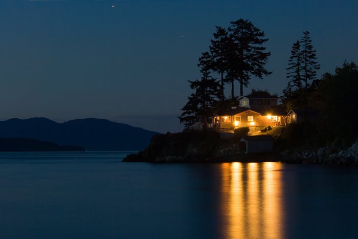 A home overlooking a lake at night with a forest in the background.